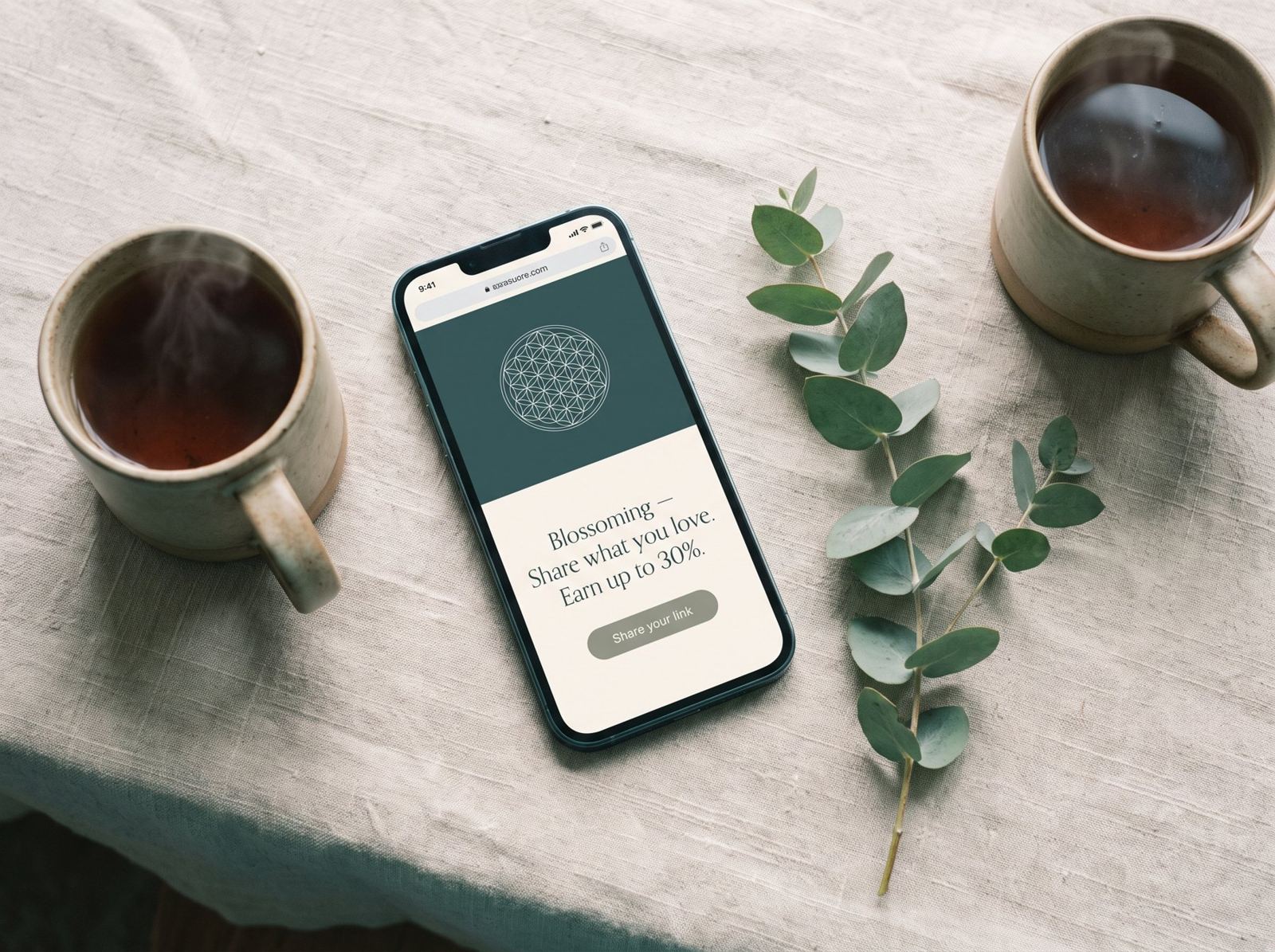 A phone between two cups of tea, open on the Blossoming affiliate page — share what you love, earn up to 30%